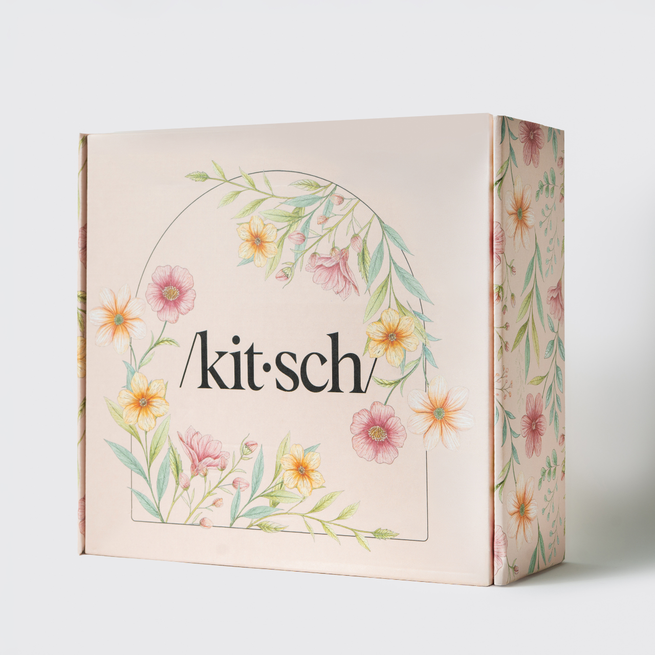 KITSCH Mother's Day Box gift box close-up — front and side view of blush pink /kit·sch/ gift box with watercolor floral wreath design featuring pink, orange, and yellow flowers with green botanical leaves — premium Mother's Day hair & beauty gift set packaging