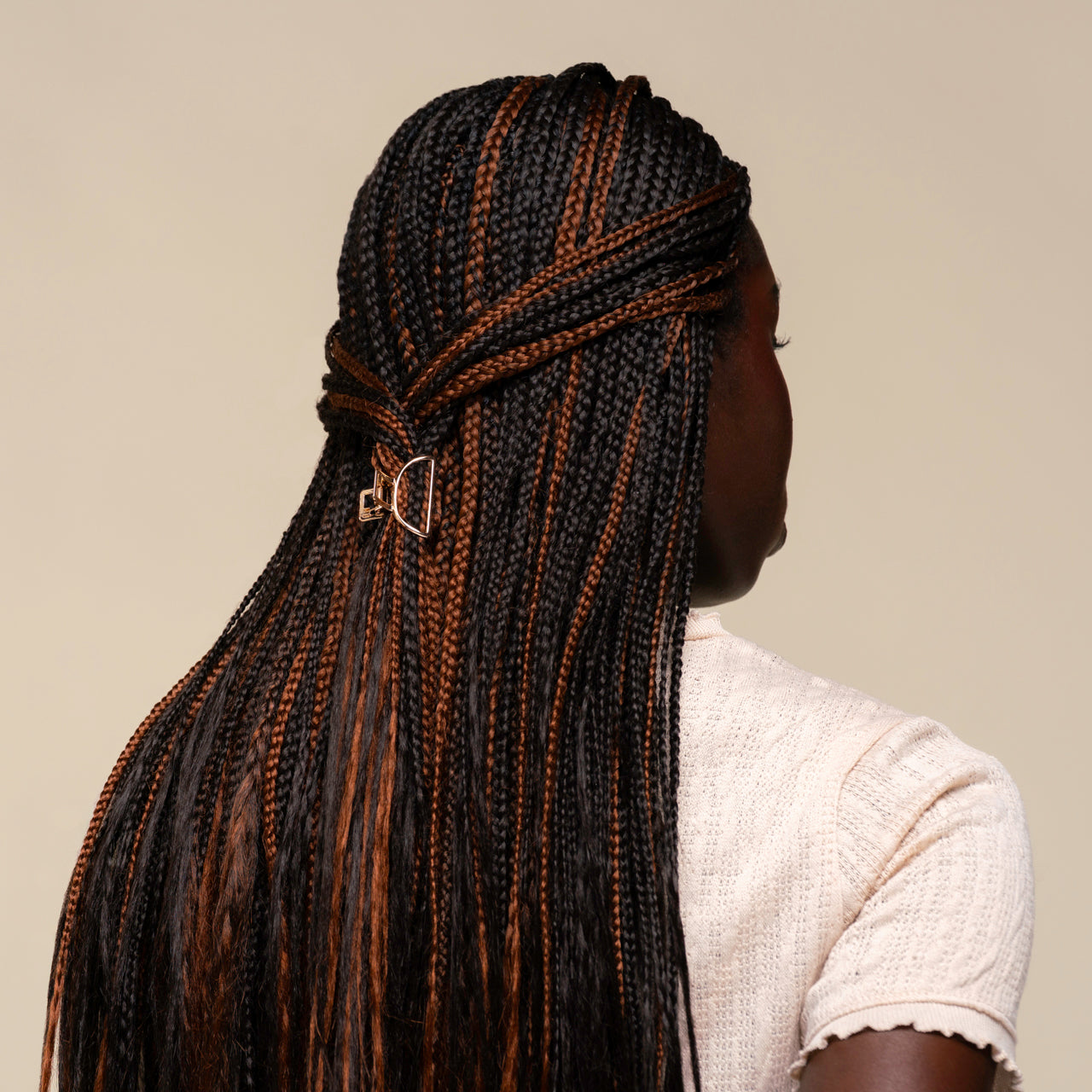 Person with mirco braids styled in a mini gold claw clip against a neutral background