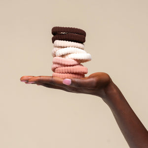 Stack of kitsch blush ribbed elastic hair ties held in a hand against a beige background