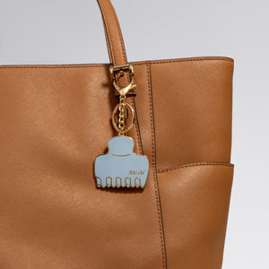 Brown leather handbag with Metal enamel keychain of the kitsch Haze Blue Cloud Clip  on a light gray background