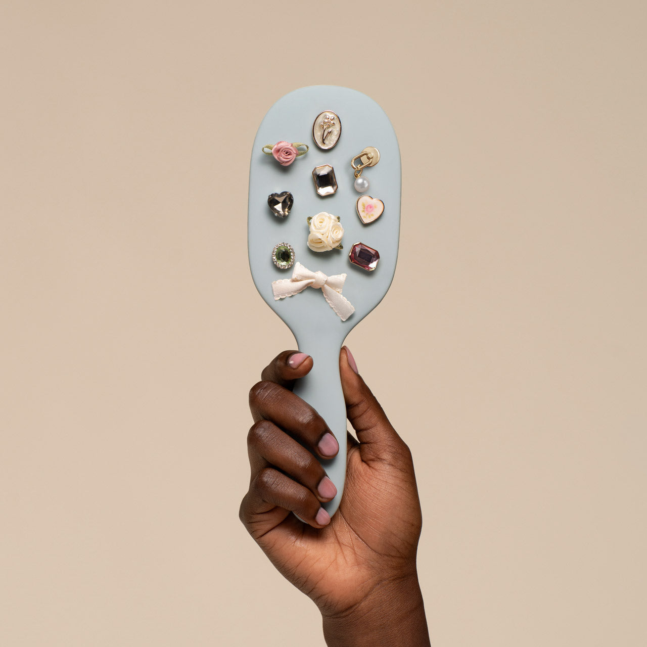 Hand holding a paddle brush with decorative pins against a beige background