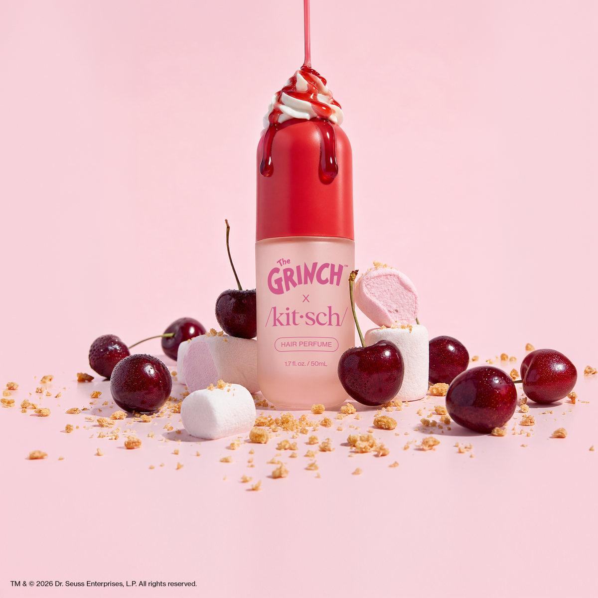 The Grinch x Kitsch Cherry Cheer Hair Perfume bottle topped with whipped cream and cherry syrup among cherries and marshmallows