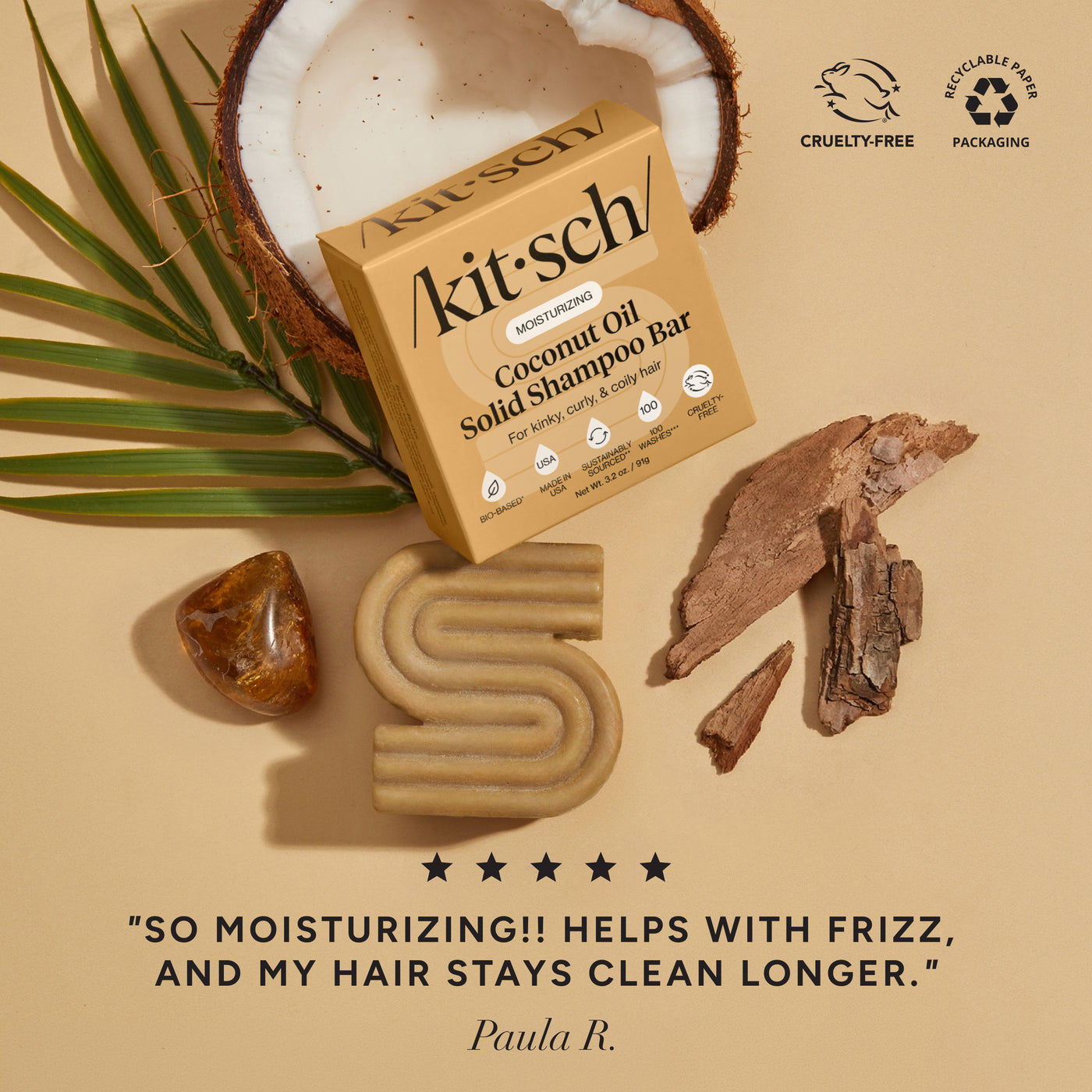 KITSCH Coconut Oil Solid Shampoo Bar — ingredient flat lay on warm tan background with coconut, palm leaf, amber stone, and driftwood — 5-star review: SO MOISTURIZING!! HELPS WITH FRIZZ, AND MY HAIR STAYS CLEAN LONGER. — Paula R. — Cruelty-Free | Recyclable Paper Packaging — Deeply cleanses and moisturizes kinky, curly, and coily hair from roots to ends