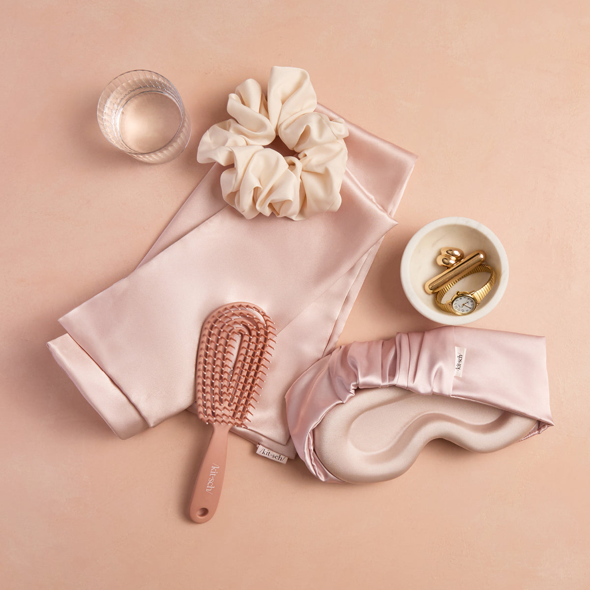 KITSCH Blush Contour Pillow Eye Mask — blush eye mask styled with a satin pillowcase, scrunchie and brush on a peach surface — soft satin adds a touch of luxury to your bedtime routine — a full satin sleep set